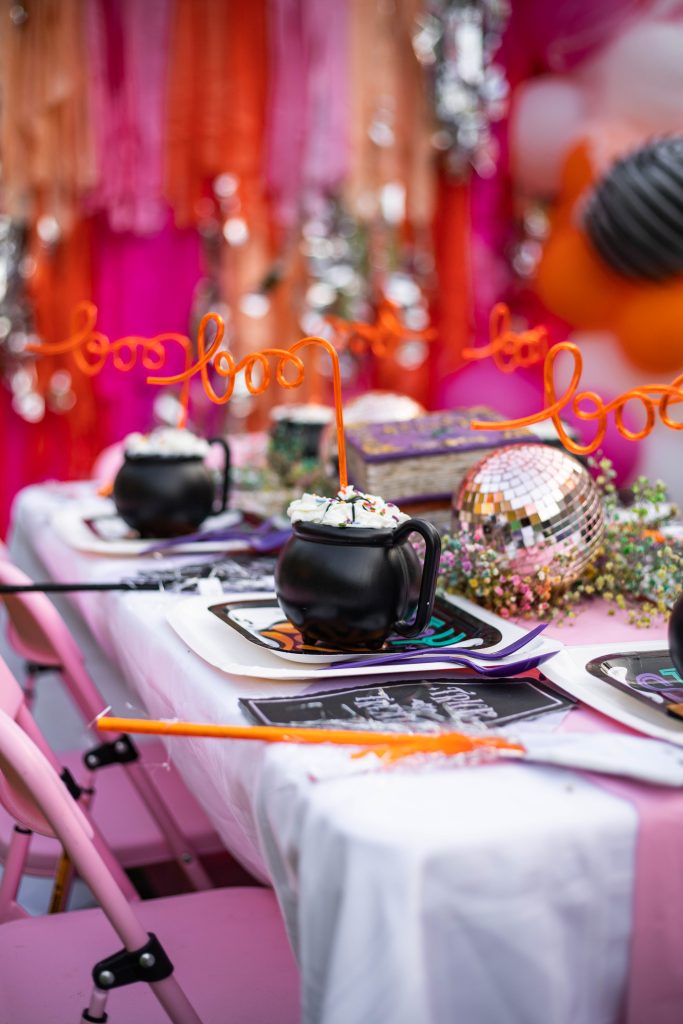 Halloween party table with cauldron cups, ghost wands, and fringe backdrop