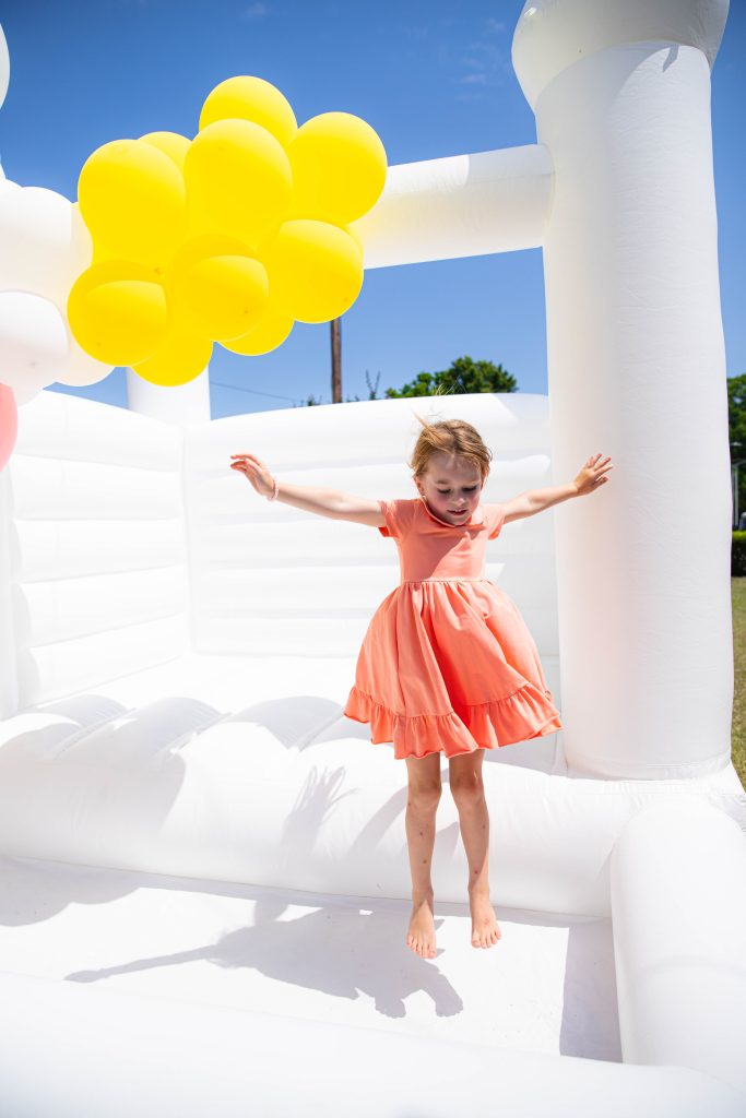 little girl at squeeze the day party in white bounce house and orange dress on
